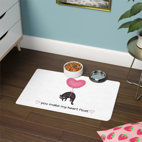 White mat with a heart and black cat illustration and text on a wooden floor.