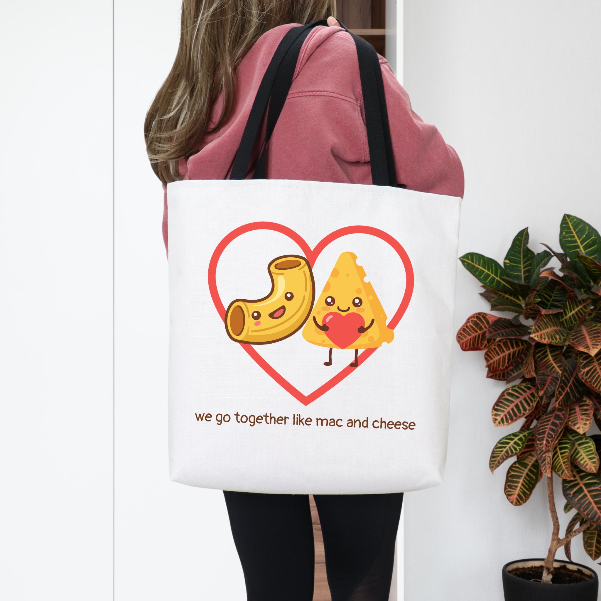 Person holding a tote bag with mac and cheese design and text.