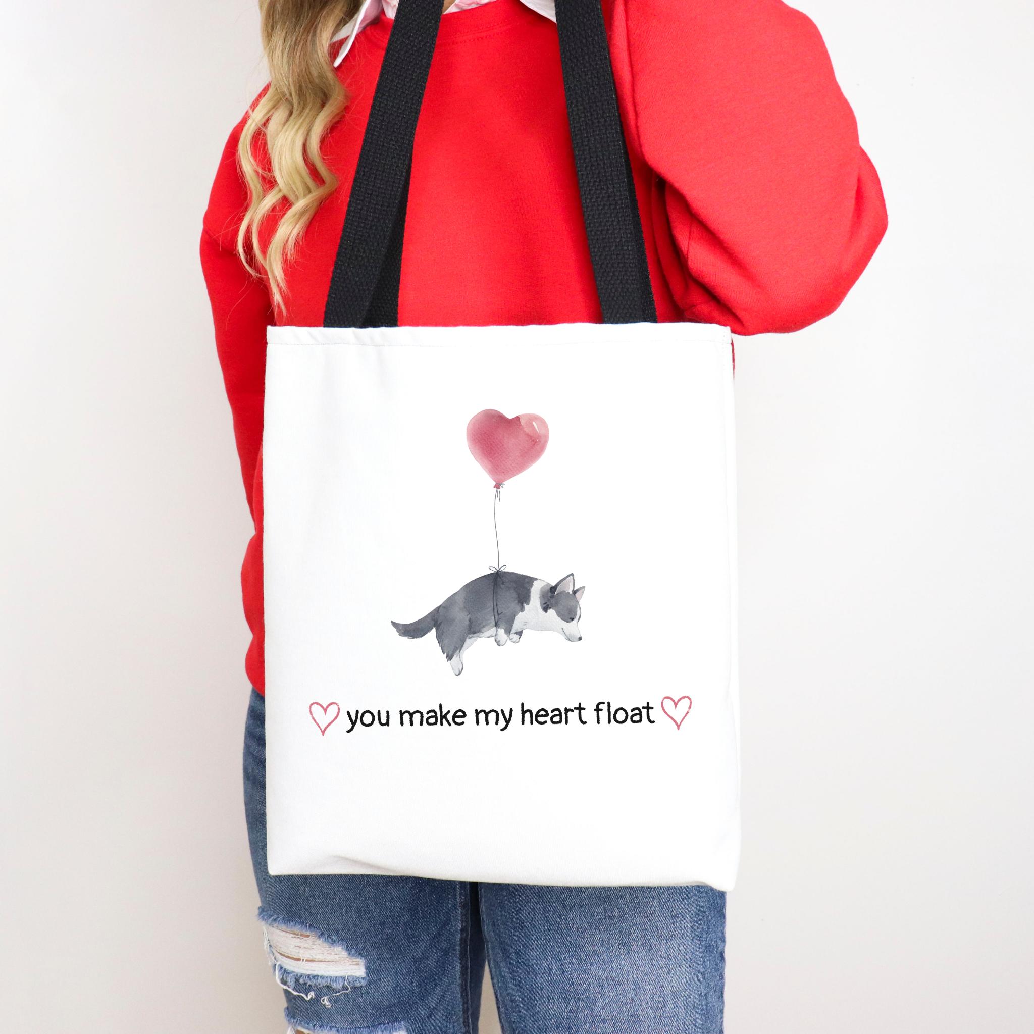 Person holding a tote bag with a puppy and heart design and text 'you make my heart float'.